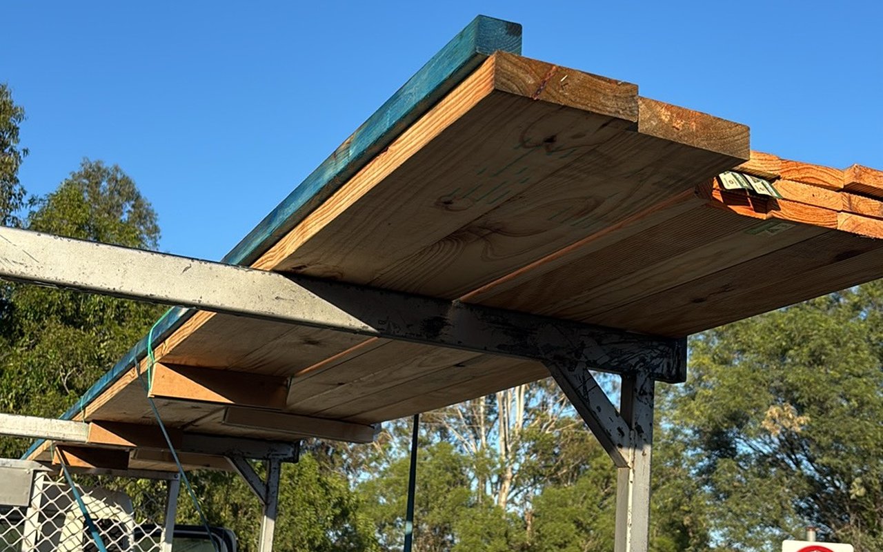 Long timber lengths strapped on a ute's ladder rack against a clear blue sky